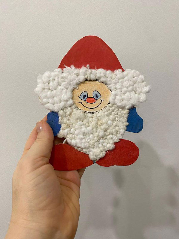 Детская новогодняя поделка — Санта из бумаги и ватных шариков, которую держит рука автора; фото крупным планом, видно текстуру.