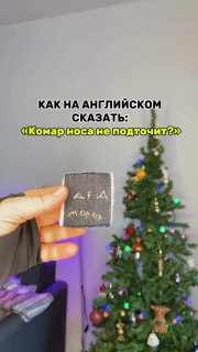 Рука держит небольшой предмет на фоне украшенной рождественской ёлки; на изображении текст вопроса «Как на английском сказать?», учебный контекст.