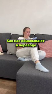 Женщина сидит на сером диване в домашней обстановке; на кадре яркая надпись «Как нас обманывают в переводе», фрагмент видео о типичных ошибках перевода.