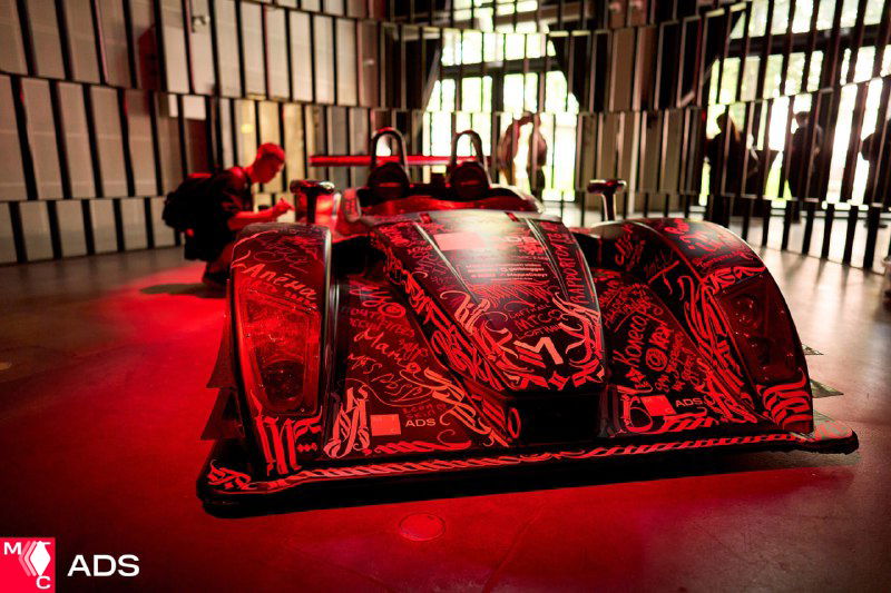 Выставочный прототип автомобиля в зоне мероприятия: низкий ракурс, яркая красная подсветка и графический декор на корпусе.