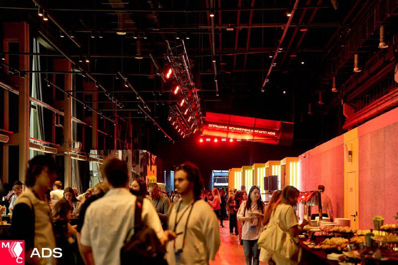 Зона фуршета и нетворкинга на конференции: гости общаются у столов с закусками, свободное перемещение по площадке.