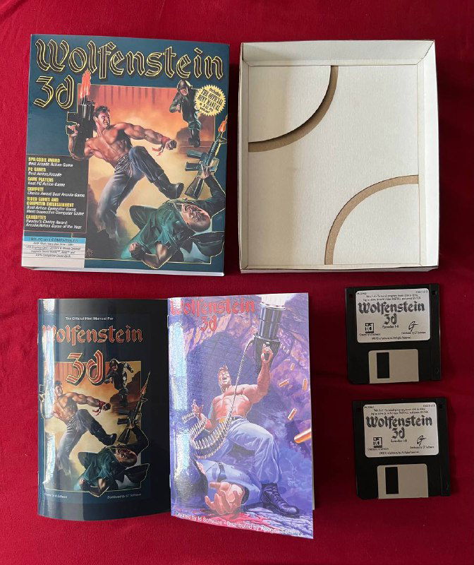 Фото коллекционного комплекта Wolfenstein 3D: открытая коробка, буклет с иллюстрациями и три 3,5-дюймовые дискеты на красном фоне, сохранность упаковки заметна.