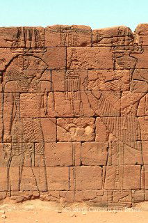 Крупный план каменной резьбы: фигуры богов и символы в нубийской традиции, стиль близок к египетской и отражает культовую сцену храма.