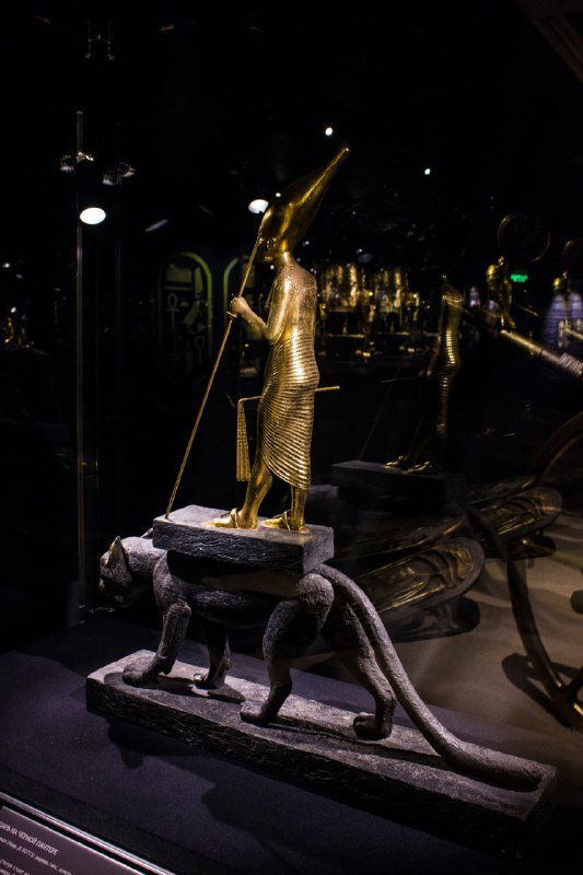 Фигура божества, стоящего на пантере/леопарде, на каменном основании в музейной витрине — ракурс демонстрирует опору и позолоту статуи.