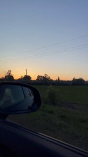 Закат над полем, снятый из машины: обочина, линии электропередачи и силуэты деревьев на фоне мягкого вечернего неба.
