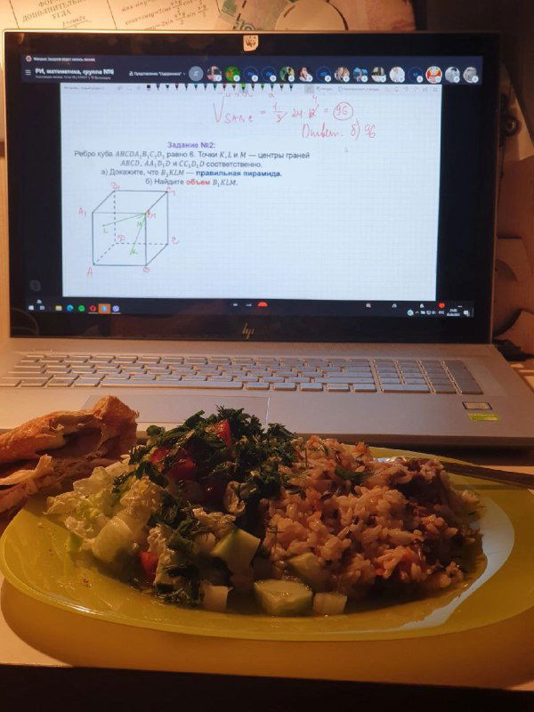 Порция обеда на пластиковой тарелке на столе перед ноутбуком с заметками и схемой на экране — комбинирование приёма пищи и дистанционных занятий.