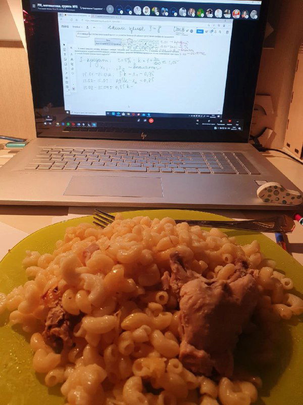 Макароны с кусочком мяса на тарелке рядом с ноутбуком, на экране видны рукописные записи — кадр показывает реальность учебных перекусов.