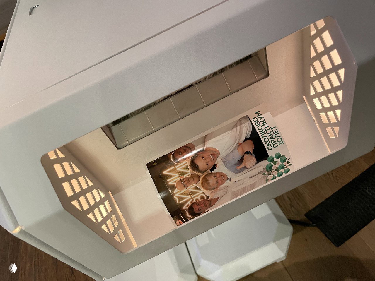 Вид сверху на внутреннюю часть фотостойки MixUp с напечатанными свежими фотографиями, демонстрирующими групповой портрет гостей и брендированный макет.