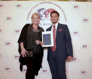 Фотография с вручением сертификата на фоне брендвола, рядом стоит человек в костюме; кадр показывает деловой контекст мероприятий и промо‑атрибутику