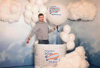 Гостиная сцена 3D-фотозоны: человек в декоративной корзине с воздушными шарами и облачными декорациями, виден брендовый принт на корзине.