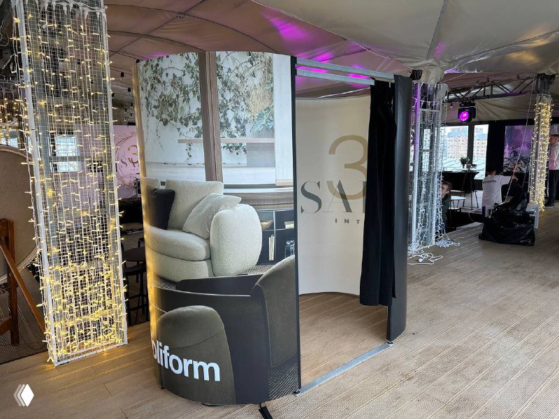 Фотобудка со шторкой в интерьере мероприятия, вид сбоку на вход и внутреннюю зону съёмки; заметен брендинг и украшения.