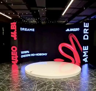 Интерактивная фотозона со круглой белой платформой в тёмном зале, окружённая LED‑экранами с логотипами и неоновым элементом сердца.