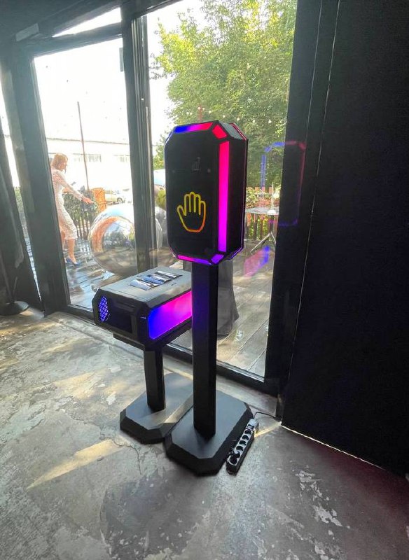 Сенсорная стойка Tech-Scan в интерьере: высокий черный корпус с подсветкой и иконкой ладони на панели, установка для ивента рядом с окном.