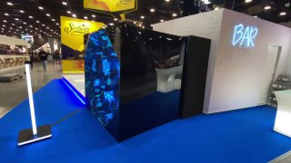 Установка фотозоны «Калейдоскоп» на выставочном стенде: зеркальный корпус, круглая панель входа и синий выставочный пол, вид сбоку на модуль