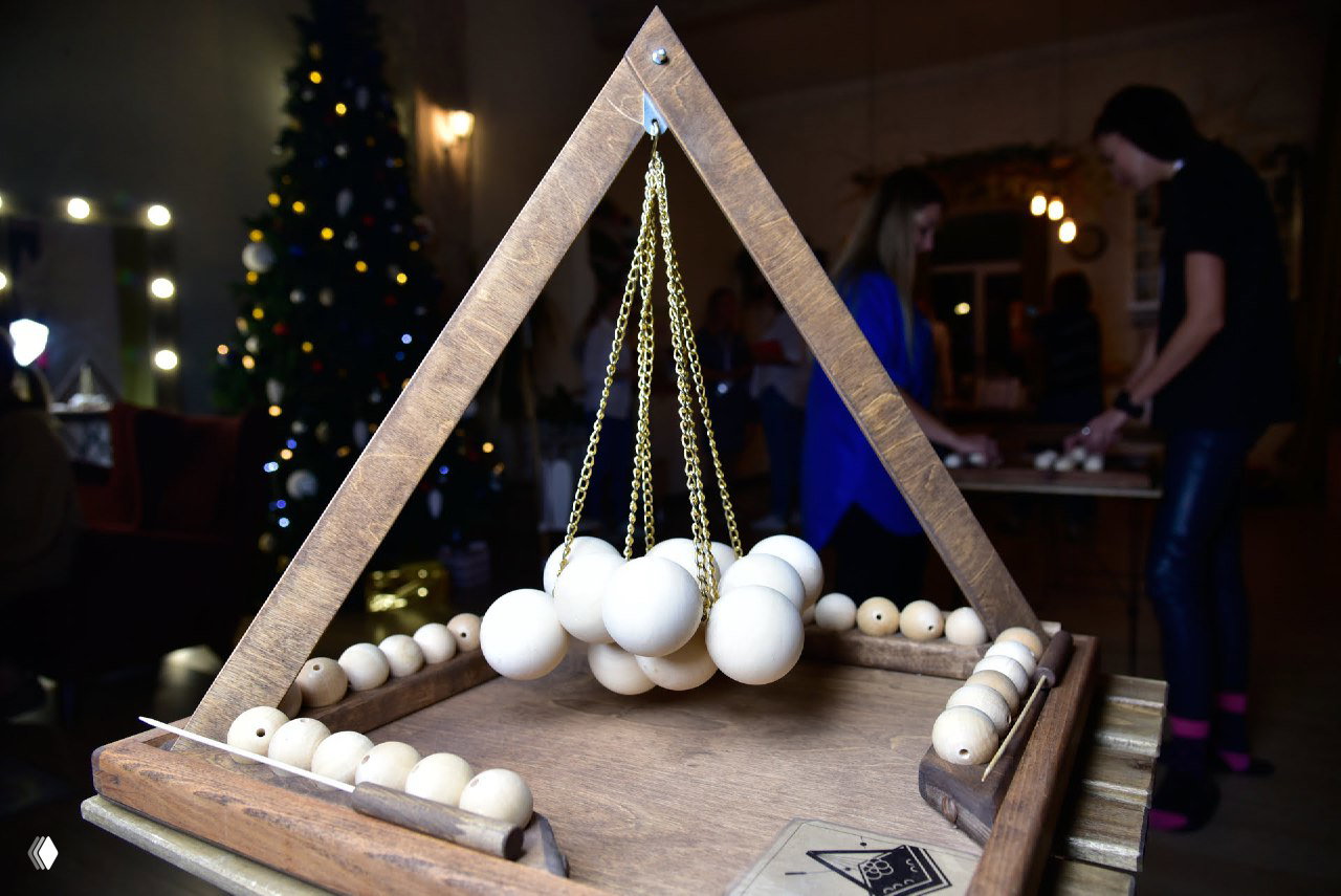 Крупный план деревянной игры с треугольной рамой и висящими шариками на цепочках — реквизит для аренды, детализация деревянной фактуры и конструкции.
