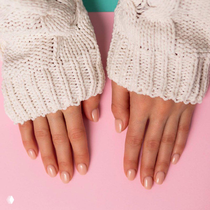 Две руки с естественным нюдовым маникюром: короткие округлые ногти в спокойном телесном оттенке, руки в светлом вязаном свитере.