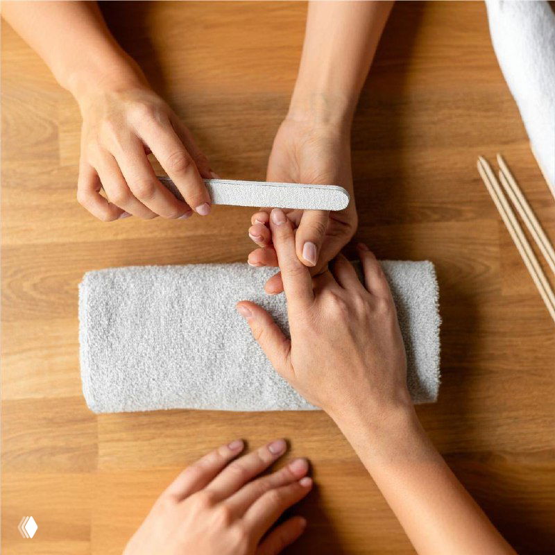 Мастер шлифует ногтевую пластину бафом, видна рабочая зона и инструменты, демонстрация техники выравнивания поверхности ногтя.