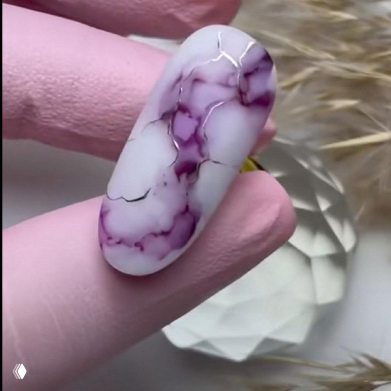 Крупный план одного ногтя с фиолетовыми акварельными прожилками на белом фоне: видна текстура верхнего глянцевого покрытия и аккуратная растушёвка пигмента.