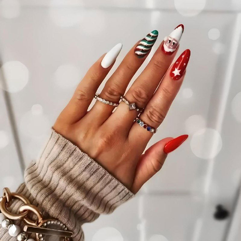 Разноцветный праздничный набор: длинные заострённые ногти с красными, белыми и зелёными элементами и маленькими рисунками, создающими новогоднее настроение.