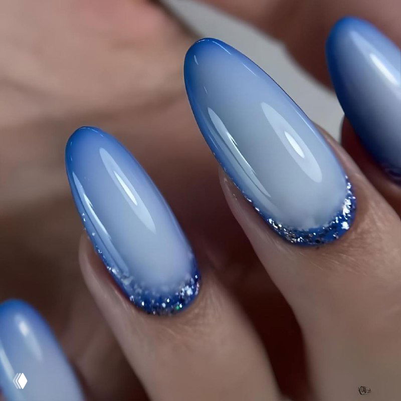 Голубой омбре-маникюр с глубокими синими кончиками и мелким блёсточным обрамлением у кутикулы — современный зимний дизайн.