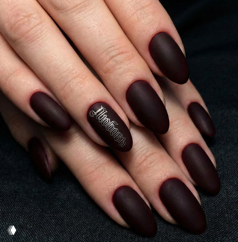 Матовые бордовые ногти глубокого винного оттенка с аккуратной готической надписью на одном из пальцев — драматичный и строгий образ.