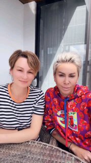 Две женщины на террасе: одна в полосатой футболке, другая в яркой худи, сидят за столом — снимок в неформальной обстановке.