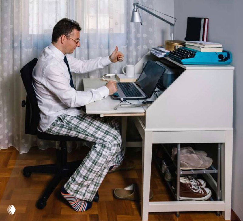 Мужчина в рубашке и пижамных штанах сидит за рабочим столом дома, подчёркивая контраст делового верха и домашнего низа при созвоне.