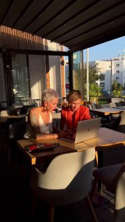 Две женщины за столом в кафе на солнечном свете: автор поста и Эльвира Фларидовна работают за ноутбуком и обсуждают расписание и дела семьи