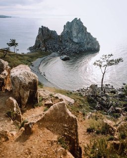 Дикая скалистая бухта на острове Ольхон с узкой песчаной полосой и редкими деревьями на фоне голубого неба