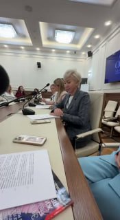 Наталья Будько за столом на заседании, говорит и читает документы; вид сбоку с микрофоном и участниками в зале Совета Федерации.