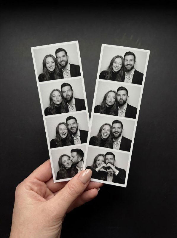 Рука держит две чёрно‑белые фотоленты с парой: по четыре кадра в каждой ленте, улыбки, поцелуй в щёку и тёплая атмоcфера на тёмном фоне.