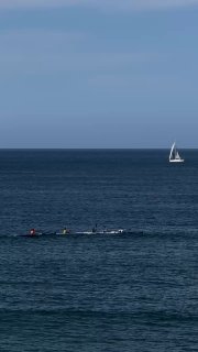 Вертикальное фото моря с парусной лодкой на горизонте и людьми в воде; спокойный морской пейзаж, подчёркивающий летнюю атмосферу поста.