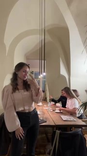 Женщина делает селфи в зале с арочными потолками: длинный деревянный стол и участницы встречи расположены вдоль него.