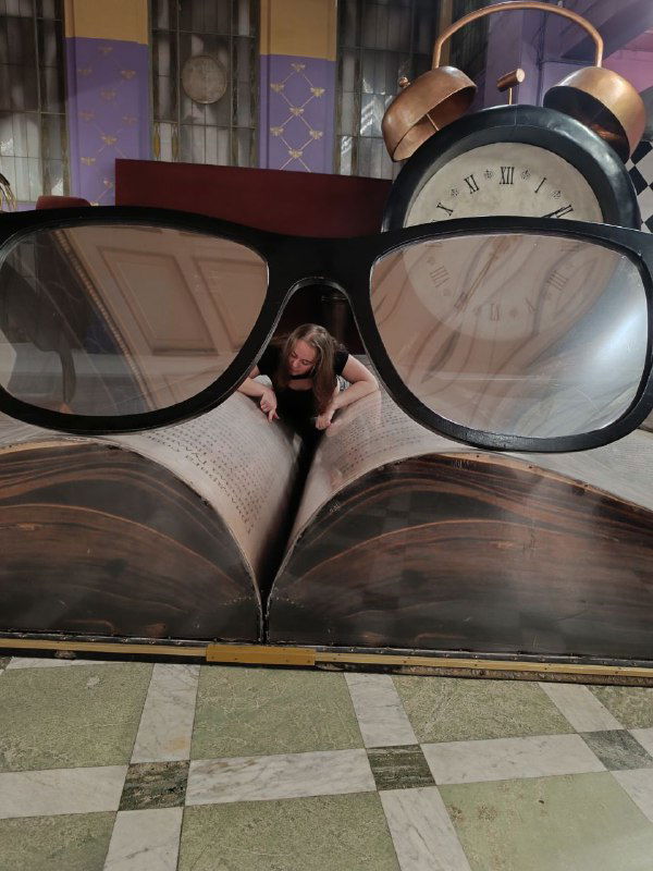 Творческая фотография в квесте: стеллаж с макетом очков и книг, через которые проходит миниатюрная фигура человека, игра с перспективой.