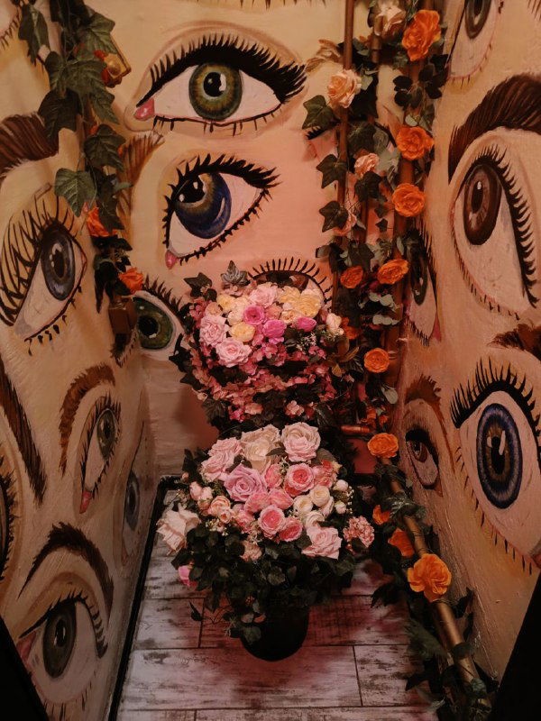 Инсталляция с множеством нарисованных глаз и букетом цветов — интерьерная фотография из комнаты квеста с художественным оформлением.