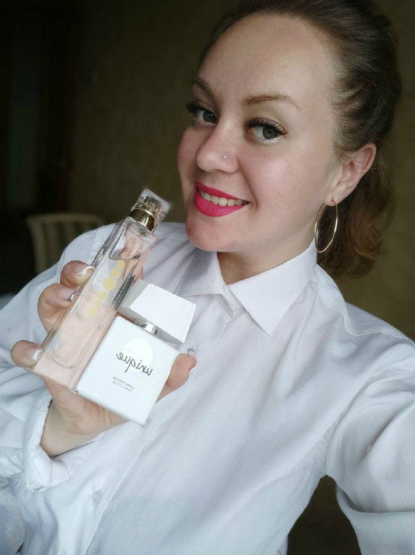 Женщина улыбается и держит флакон духов крупным планом: демонстрация товара в контексте сетевых продаж или промоакции.