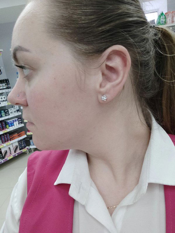 Профиль женщины в розовой фирменной форме кассира, съемка в торговой точке: виден отрезок лица и кусок униформы на фоне магазина.