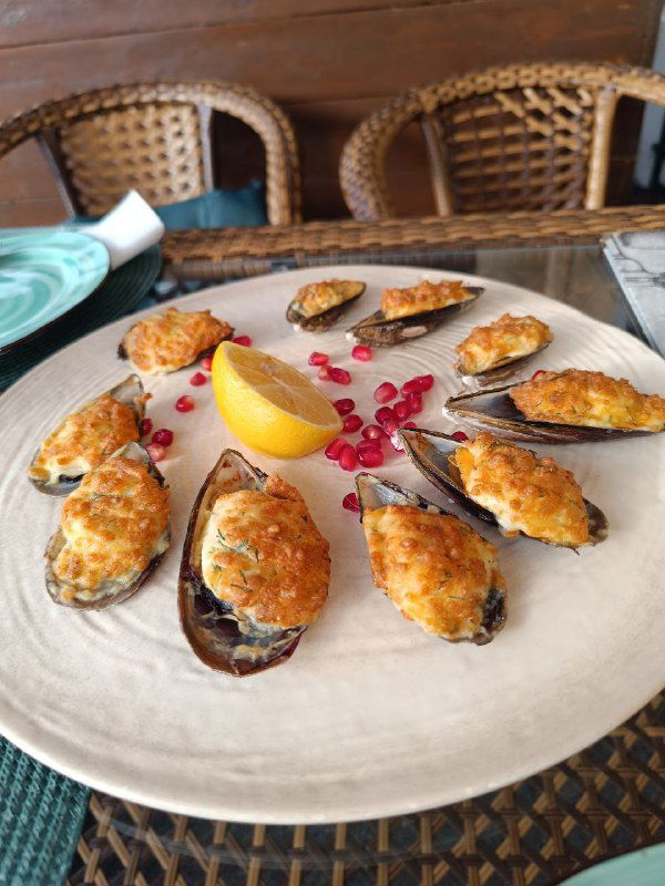 Крупный план тарелки с запечёнными мидиями, украшенной долькой лимона и зёрнами граната — аппетитная ресторанная закуска в летнем меню.