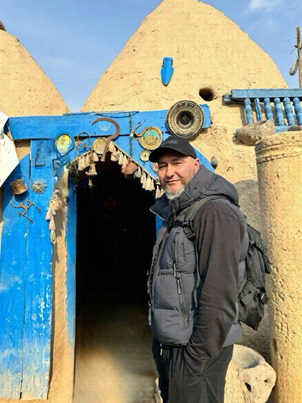 Человек в тёплой одежде стоит у ярко-голубой деревянной двери одного из харранских домов — кадр путешественника у входа в традиционное жилище.