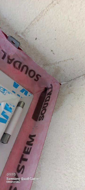 Упаковочная лента марки Соудал, частично закрывающая профиль окна; кадр крупным планом на материалы уплотнения проема.