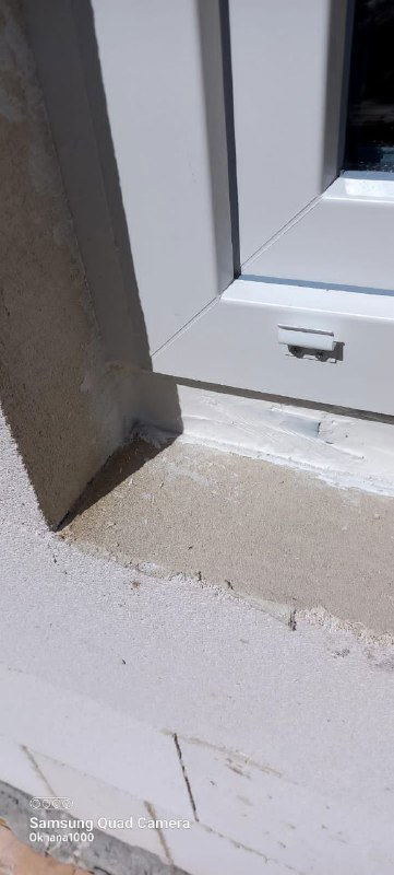 Крупный план нижней части пластикового оконного профиля, место прилегания к подоконнику и следы монтажной пены в газобетонной стене.