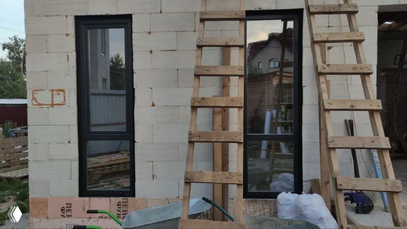 Установка высоких дверно-оконных блоков в газобетонной стене, вид сбоку с временными лесами и монтажными элементами вокруг проёма.