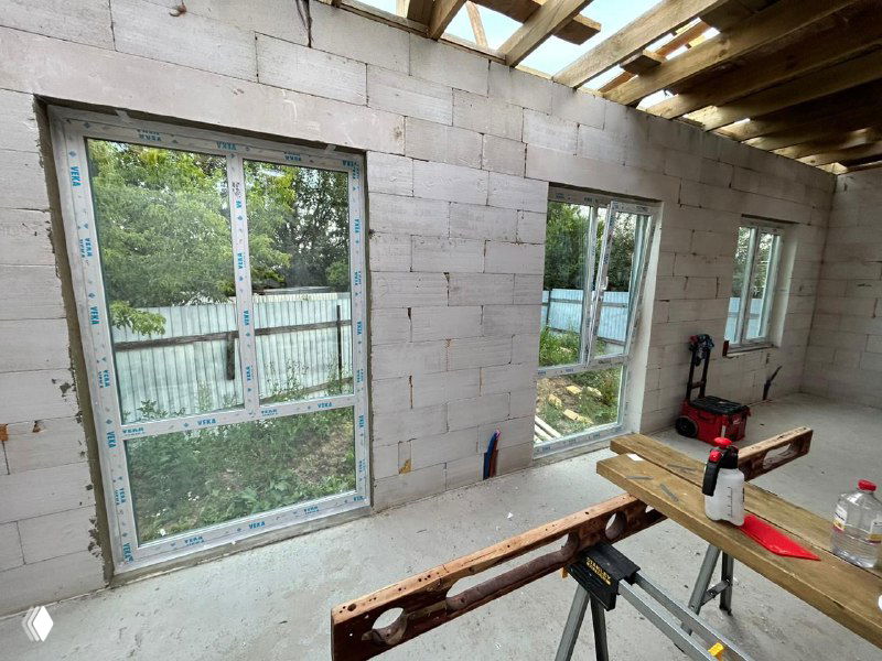 Внутренний вид на три установленных окна в газобетонной стене, рабочее место монтажников и деревянные подмости на переднем плане.