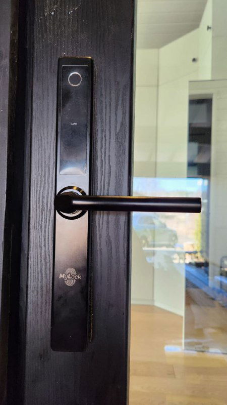 Крупный план электронного замка и черной ручки на входной двери, видно стекло и отражение инструментов и мастерской на заднем плане