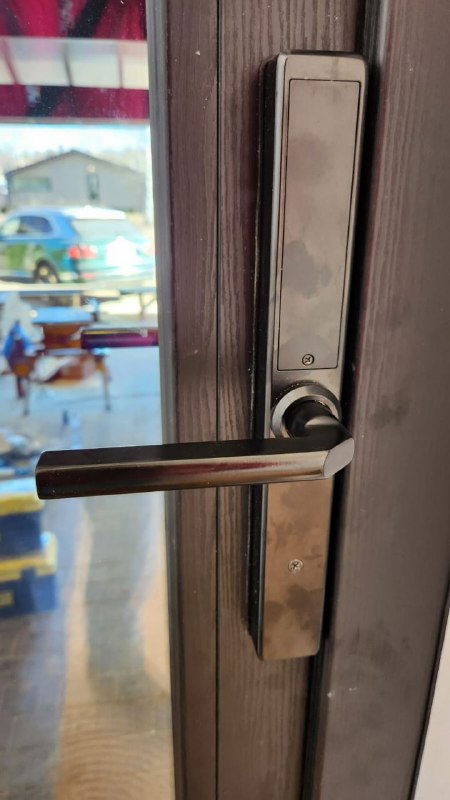 Крупный план черной ручки и петли на ламинированной входной двери, хорошо видна текстура под брашированное дерево и фурнитура