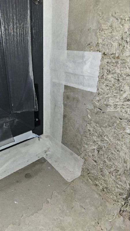 Угловой стык окна и стены с нанесенной черной парогидроизоляцией вокруг пенного шва, вид крупным планом для проверки герметичности.