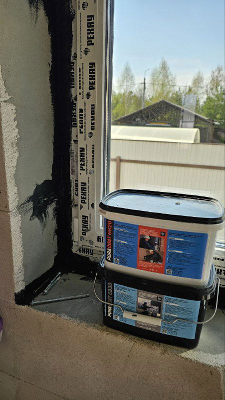 Баллон и ведро с материалами для наружной паро- и гидроизоляции на подоконнике, рядом видна нанесенная черная мастика на сопряжении шва.