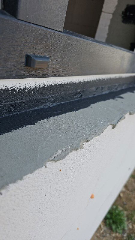 Наружный профиль рамы и полоса черного герметика вдоль наружного откоса, показано качество нанесения и примыкание к фасаду.