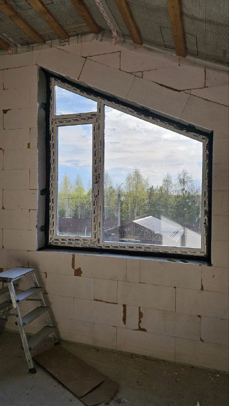 Широкий вид комнаты с установленными оконными блоками в недостроенном доме из блоков, видно форму и размещение панорамных окон.