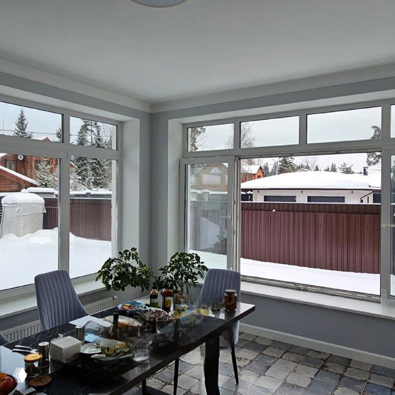 Интерьер столовой с крупными пластиковыми окнами и видом на снег во дворе — пример тёплого остекления для холодного климата.